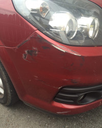 An image of a red car with a dent and scrape of the side of the bumper